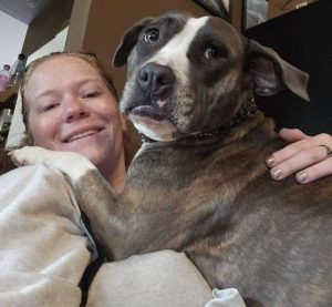 A smiling woman with a large dog hugging her.